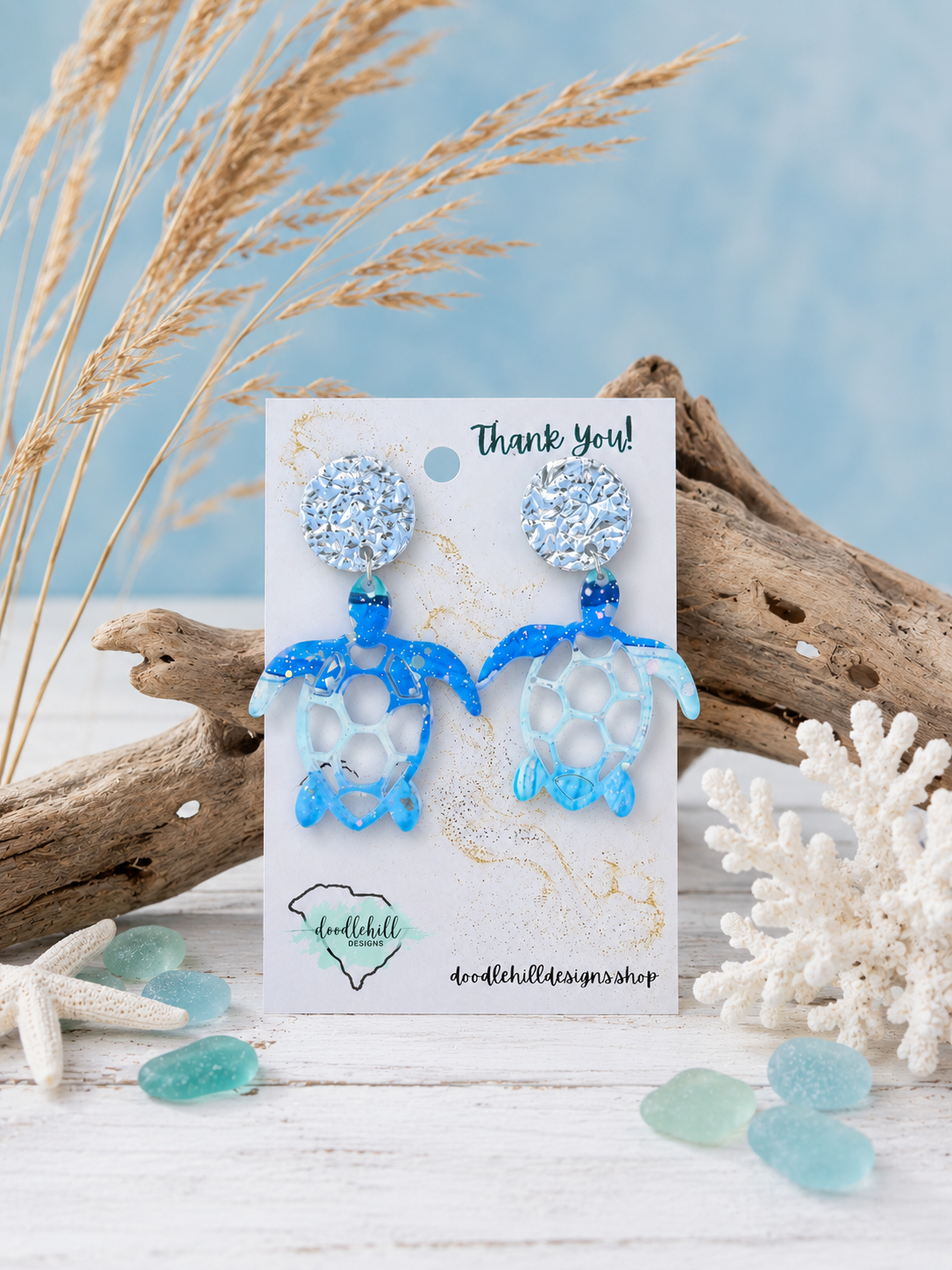 "Watercolor sea turtle acrylic earrings with silver glitter flakes and beach-inspired design displayed in a coastal product showcase."