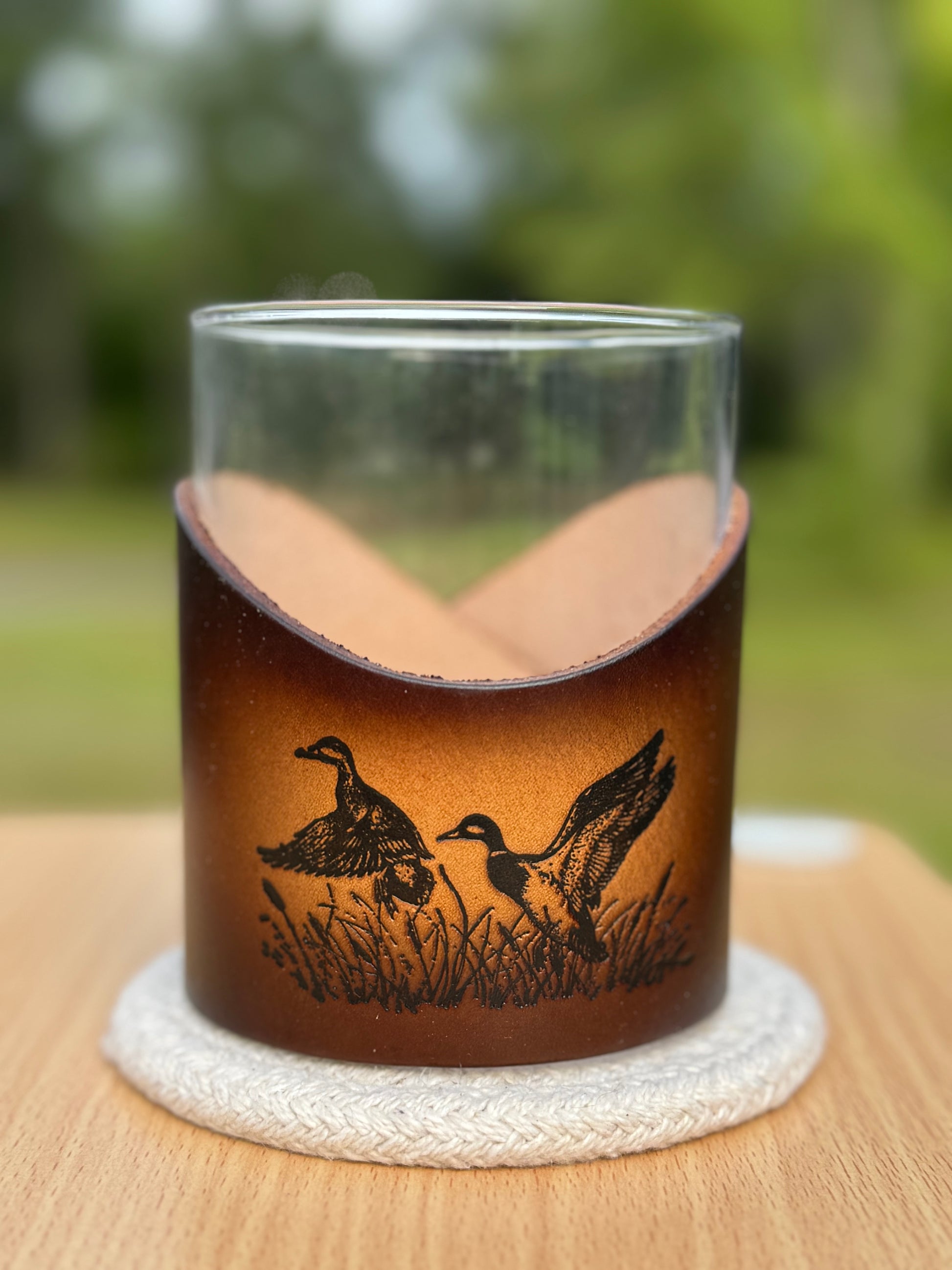 12 oz rocks glass with leather wrap. Wrap has ducks flying out of pond engraved on front of leather wrap