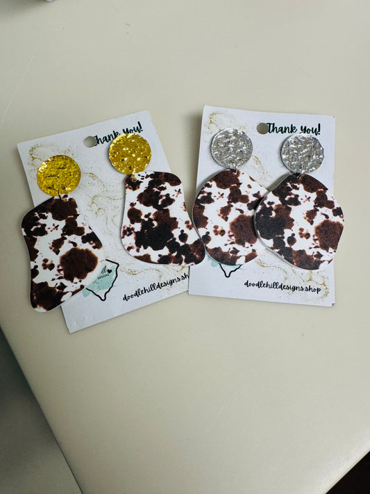 cow print earrings on white acrylic with gold  and silver textured post