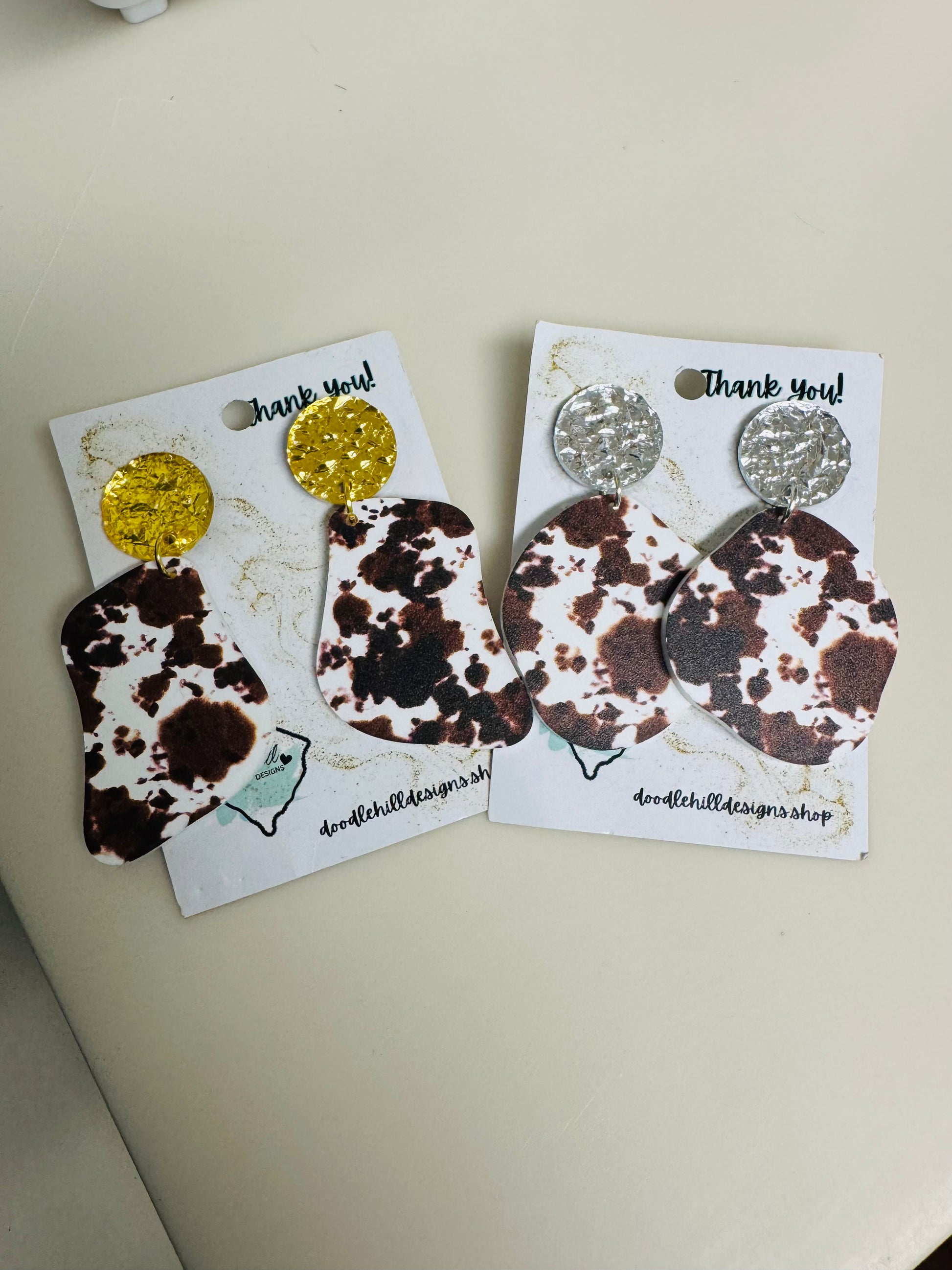 cow print earrings on white acrylic with gold  and silver textured post