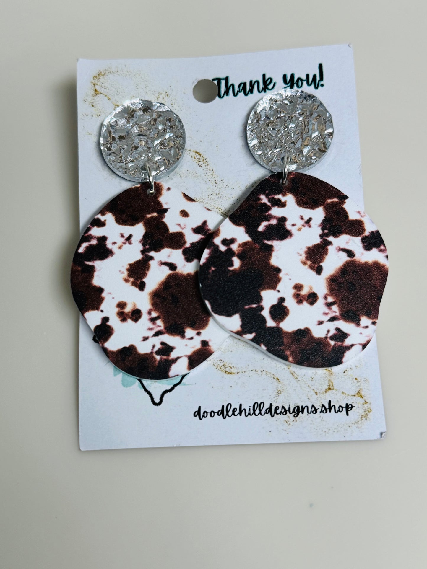 cow print earrings on white acrylic with silver textured post