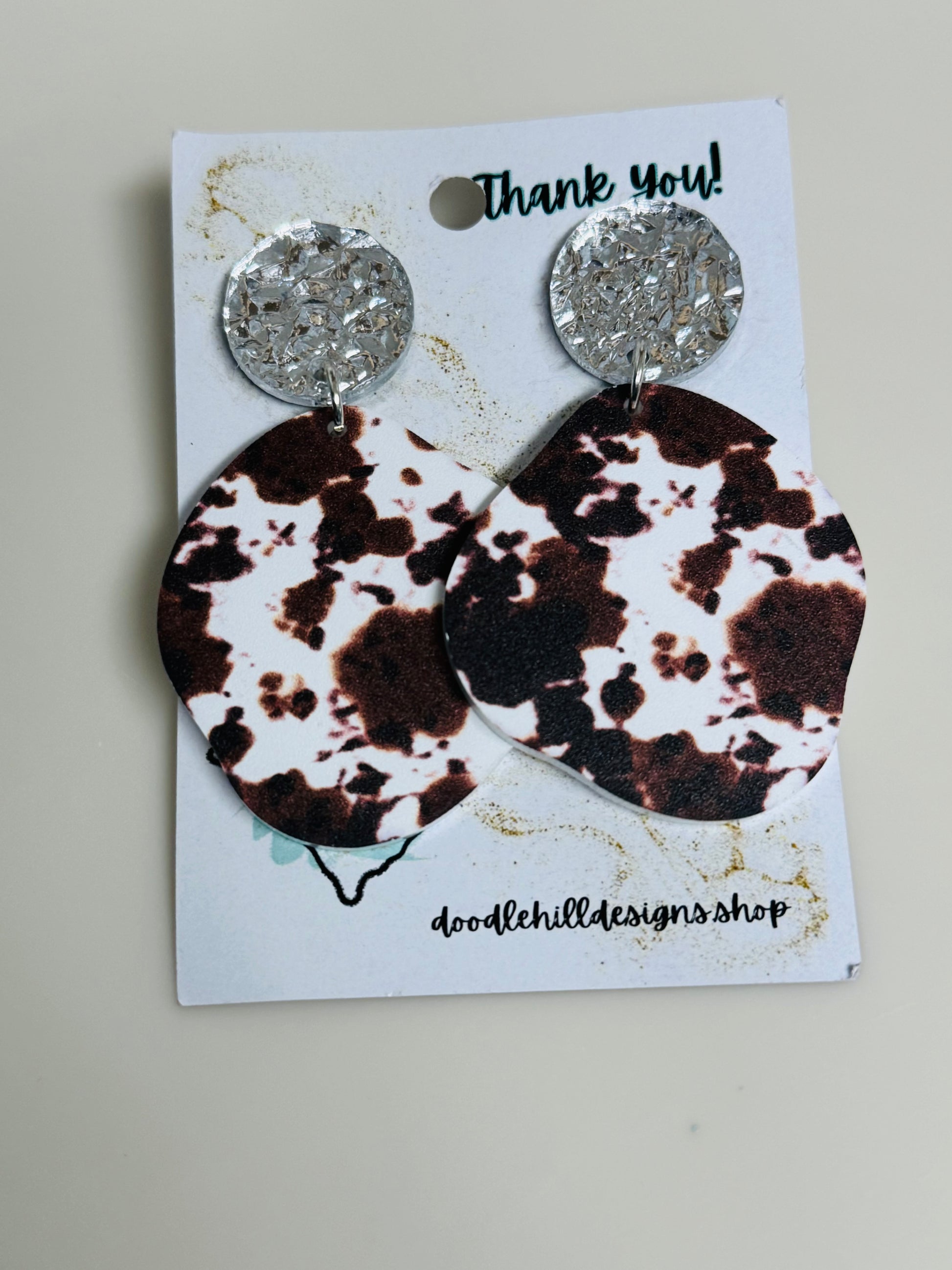 cow print earrings on white acrylic with silver textured post