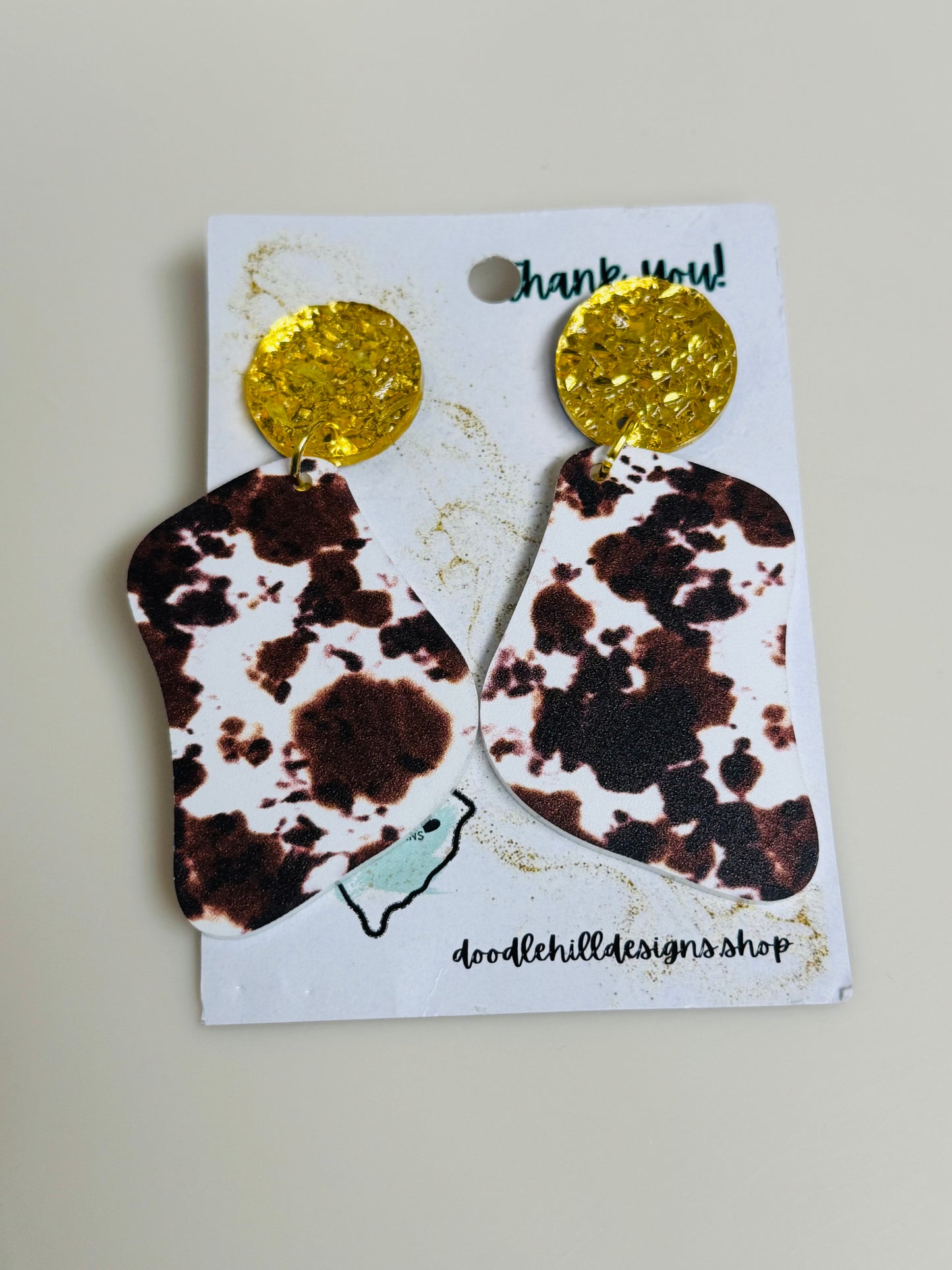 cow print earrings on white acrylic with gold textured post