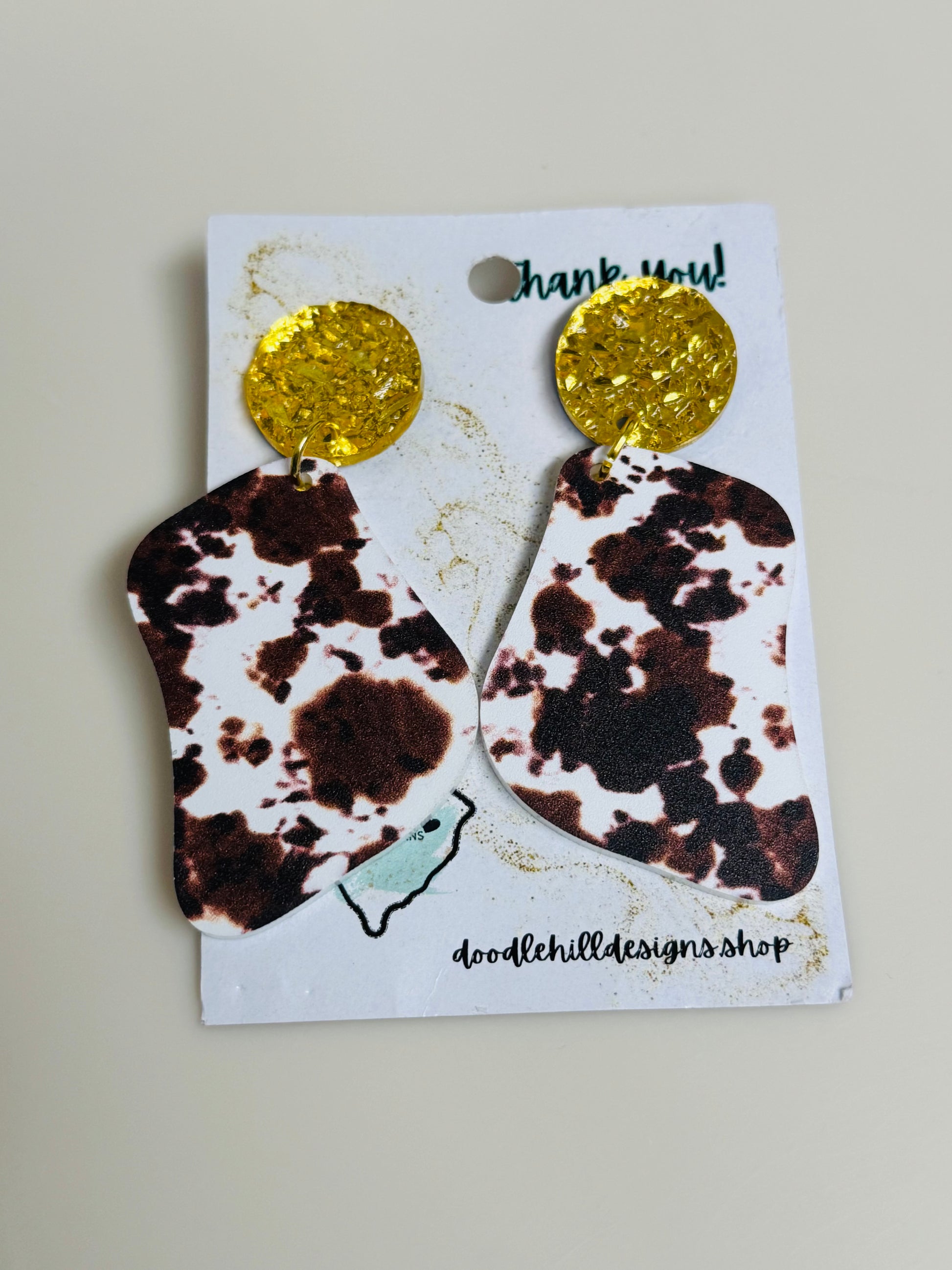 cow print earrings on white acrylic with gold textured post