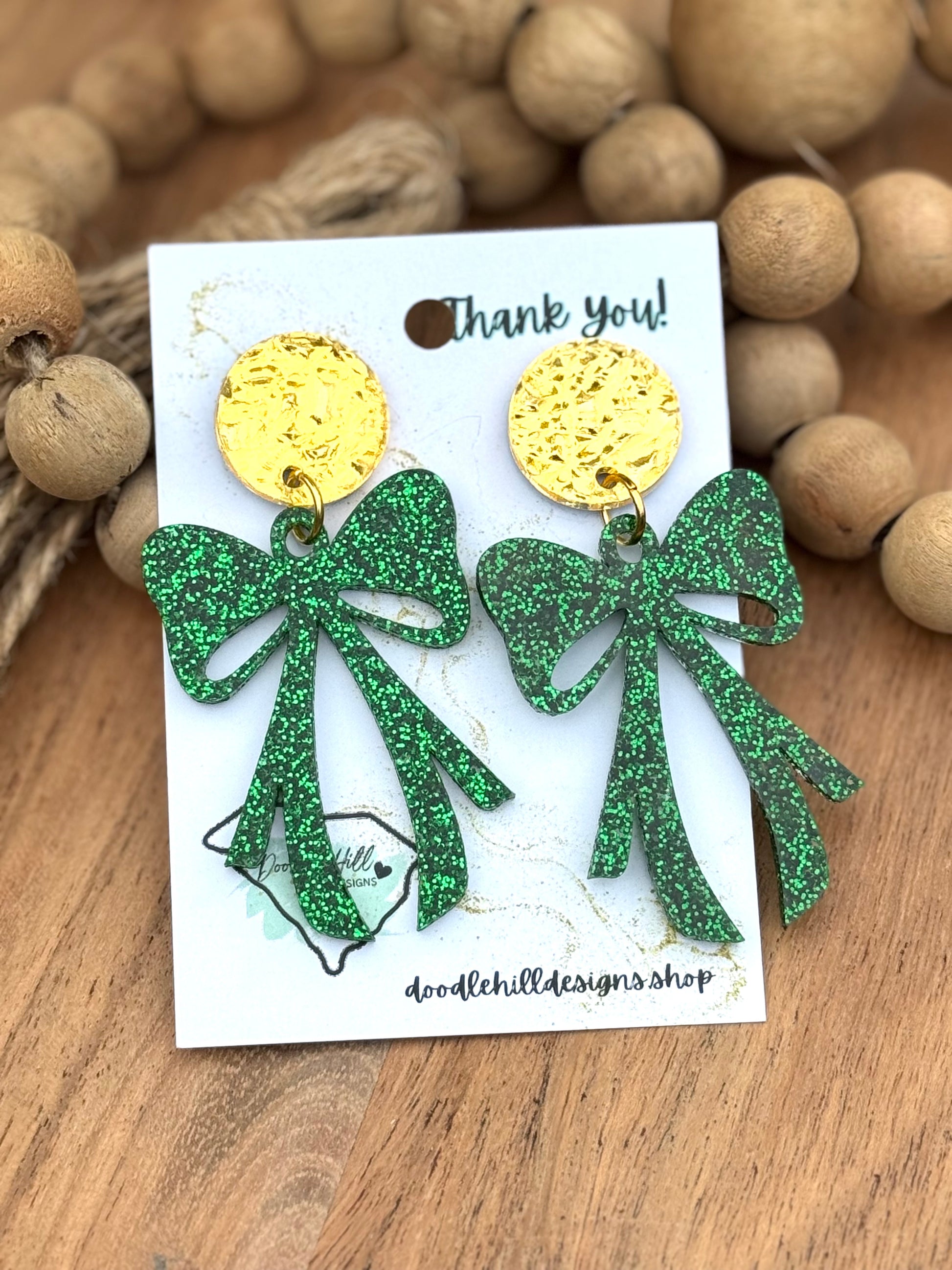Green glitter bow earrings for St. Patrick’s Day – lightweight acrylic dangle earrings with sparkling shamrock green finish. Festive statement jewelry with gold textured posts, perfect for Irish-themed outfits, lucky charm accessories, and holiday celebrations. Trendy earrings for March 17 events and everyday wear."